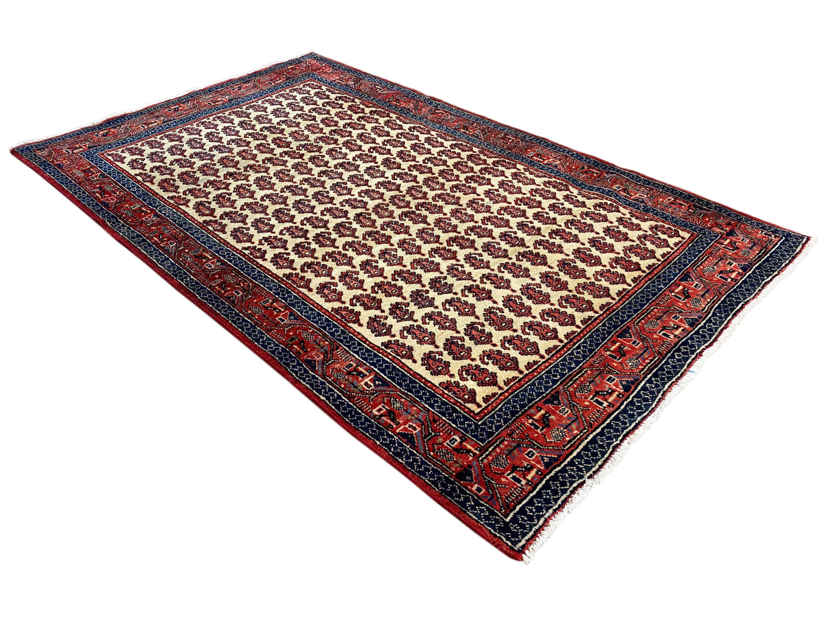 Tapis oriental crème avec bord rouge et contour bleu foncé, vue en diagonale
