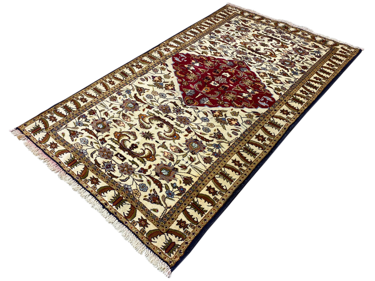 Tapis baloutche, déployé en diagonale, couleur crème avec médaillon rouge et bordure