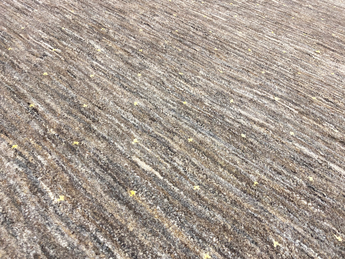 Teppichgewebe im Detail: feine melierte Linienstruktur und goldene Sprenkel.