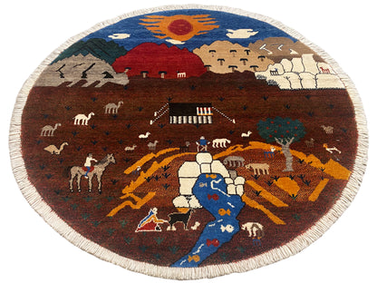 Runder Gabbeh-Teppich mit Dorfmotiv, orange-braunen Wegen und naturfarbener Umrandung
