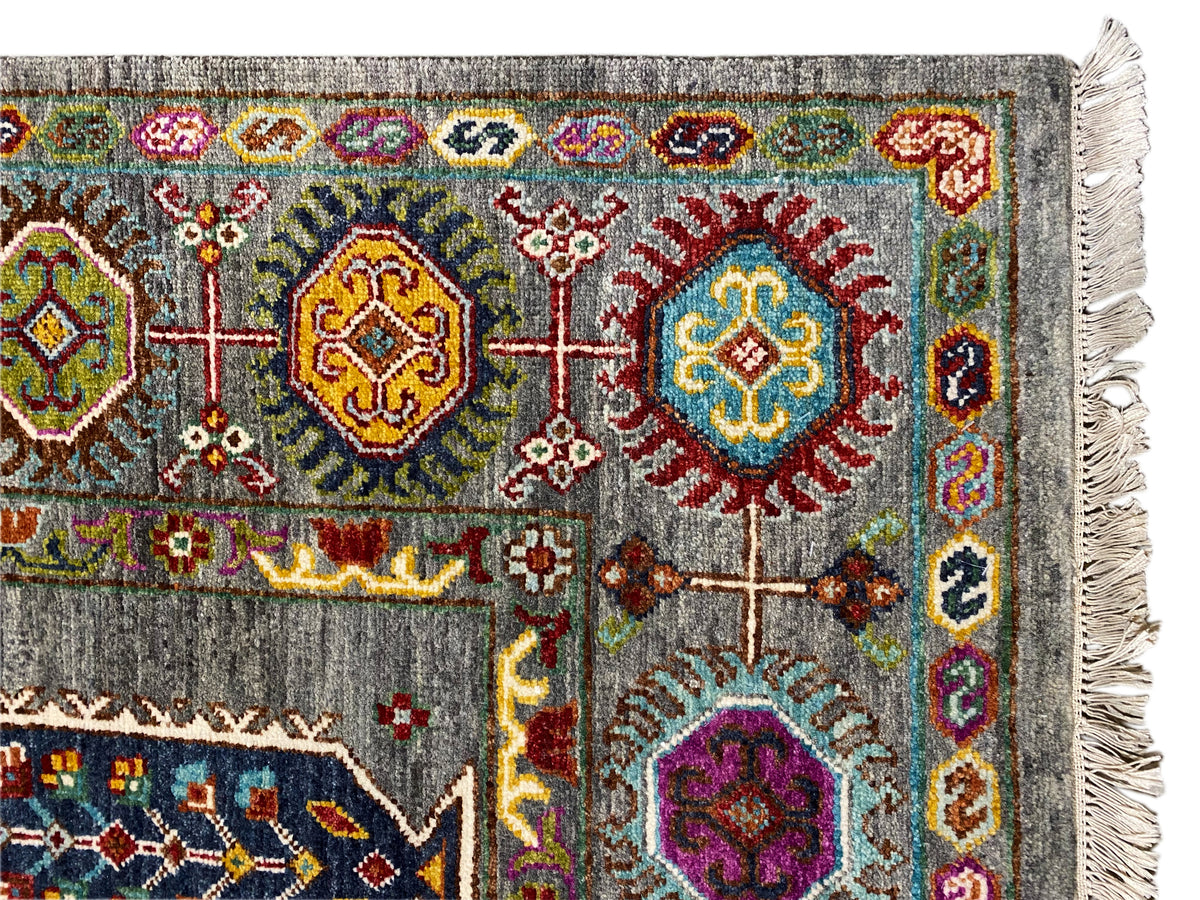 Teppich-Ecke: grauer Grund mit bunten Medaillons, Zierstreifen und Fransen.