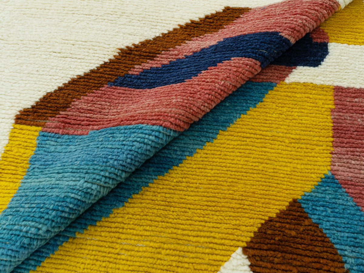 Teppich-Detail: aufgerollte Ecke mit farbigen Streifen in Gelb, Blau, Rot und Braun