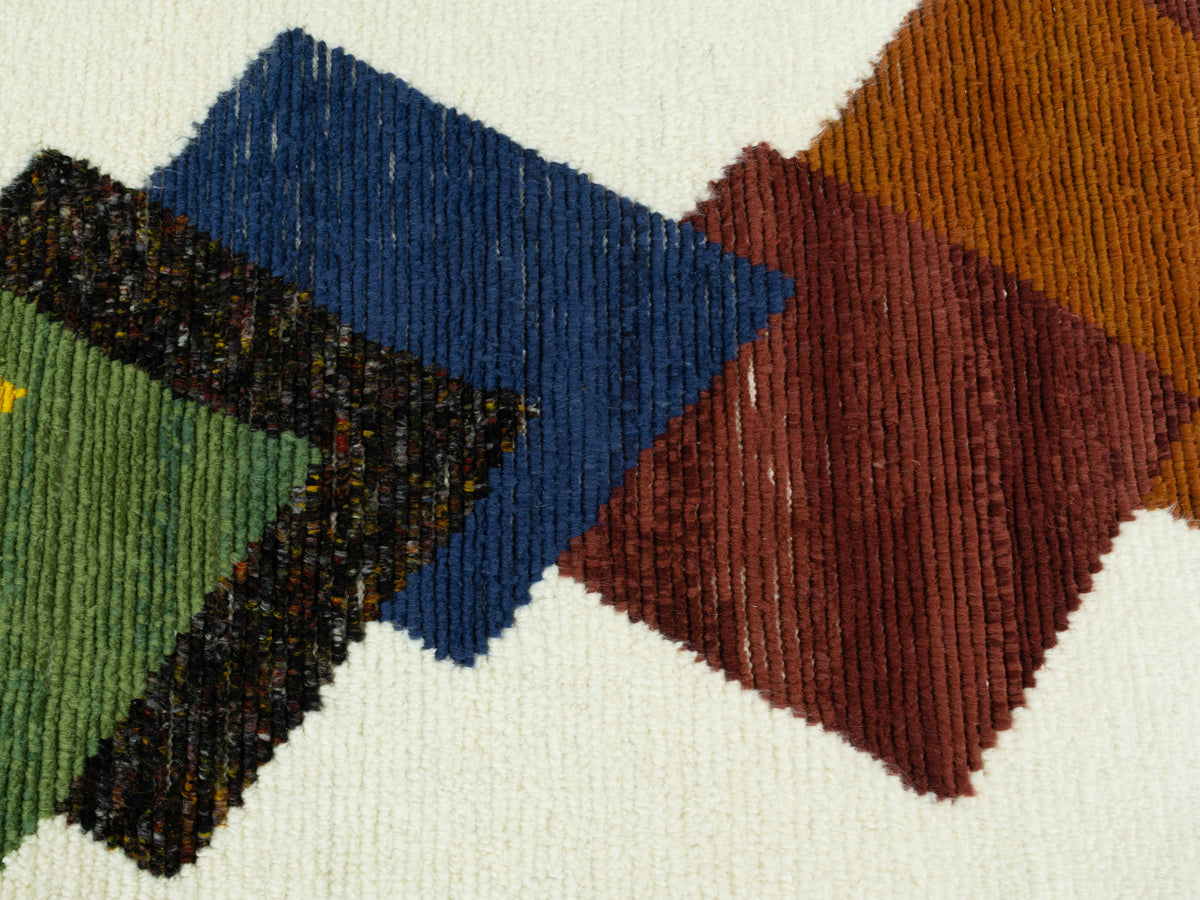 Teppichdetail mit bunten Quadraten: blaues, grünes und braunes Motiv auf hellem Untergrund