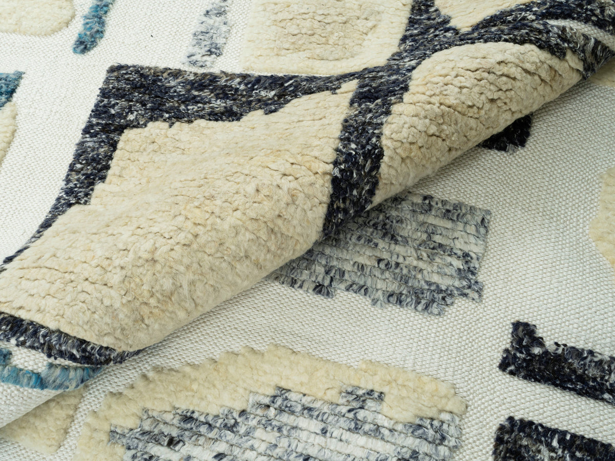 Teppich 240x170 cm Nahansicht: gepolsterte Florflächen in Creme, Blau und Schwarz, Fransen