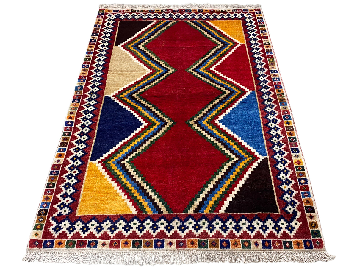 Shiraz-Teppich rechteckig mit mittigem Rautenmotiv in Rot, Blau und Beige sowie buntem Rand.